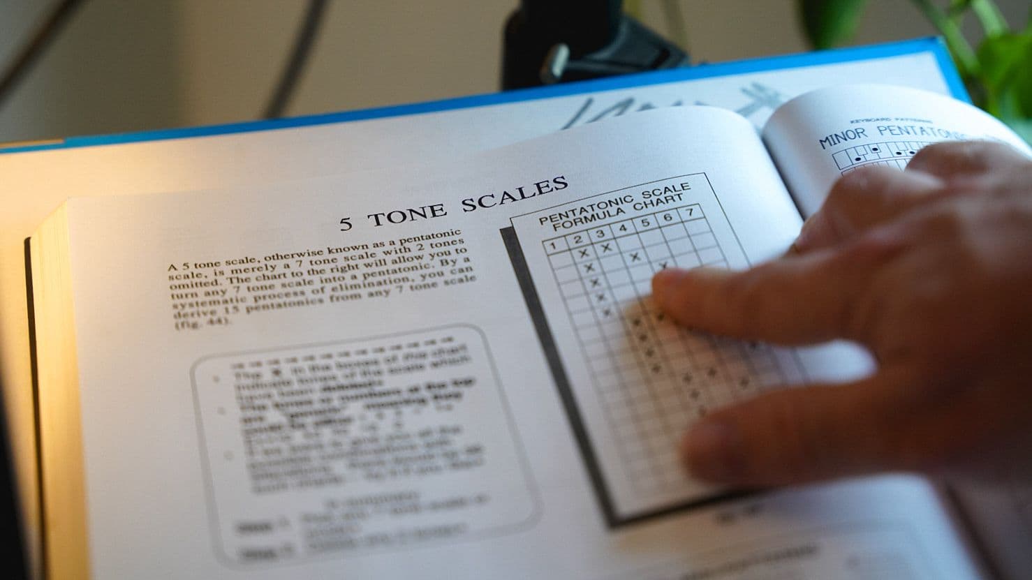 Open music theory book showing pentatonic scale charts, hand turning the page